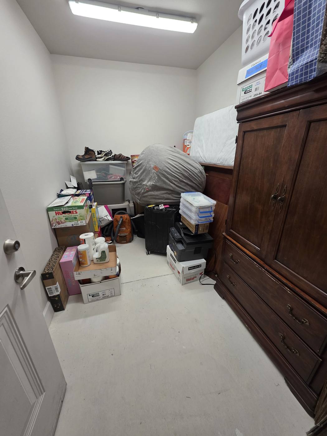 A storage room stacked with open boxes and loose items, then the same room with contents sorted and the walkway clear