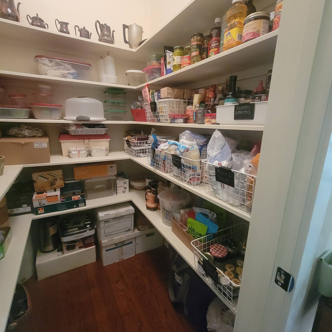 A walk-in pantry with bags and boxes piled on every shelf, then the same pantry sorted into baskets with clear zones